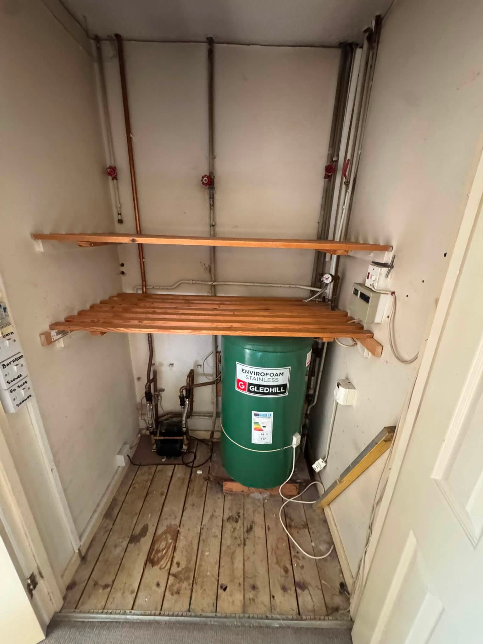 Before: the old green open-vented cylinder under wooden shelving in an airing cupboard