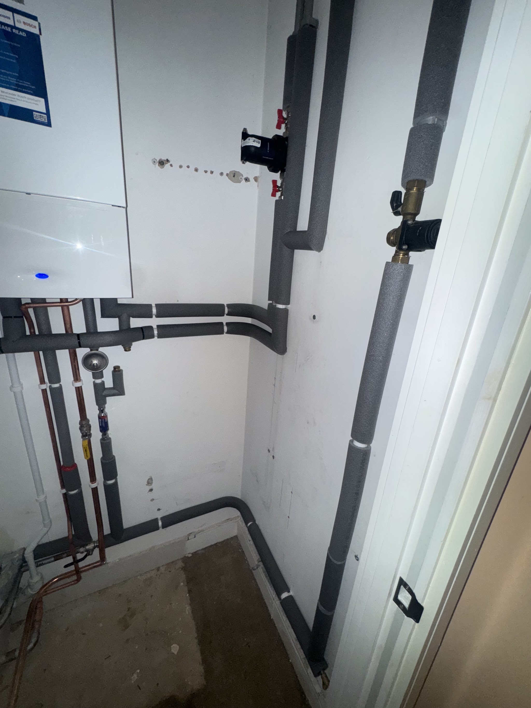 Boiler and neatly lagged grey pipe runs in a utility space