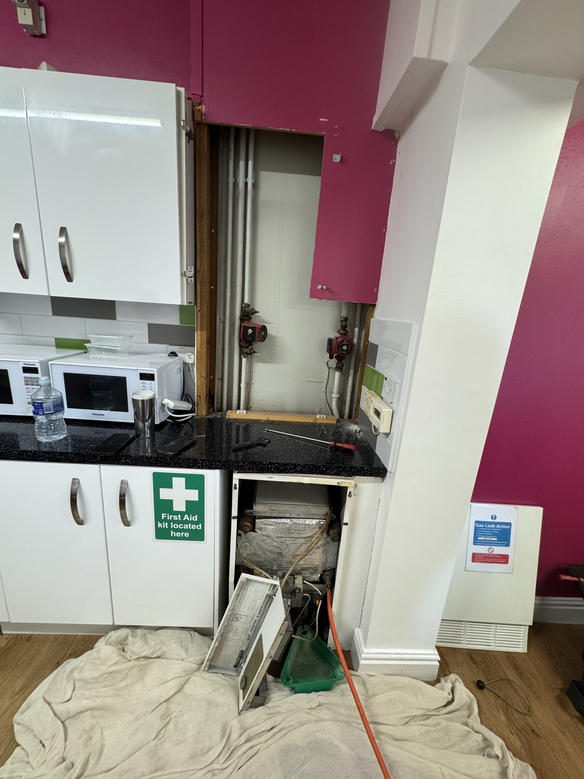 Plumbing work under a kitchen counter with dust sheets laid down